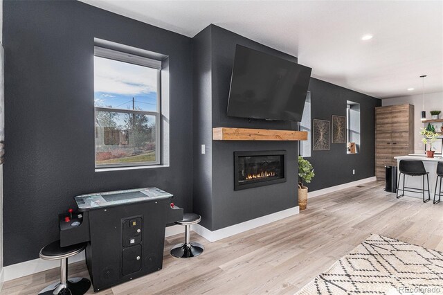 living area featuring baseboards, light wood-style flooring, a glass covered fireplace, and recessed lighting