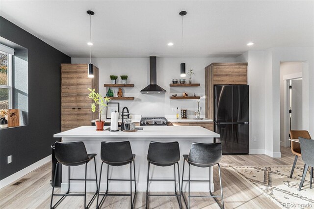 kitchen with open shelves, light countertops, a kitchen bar, wall chimney exhaust hood, and freestanding refrigerator