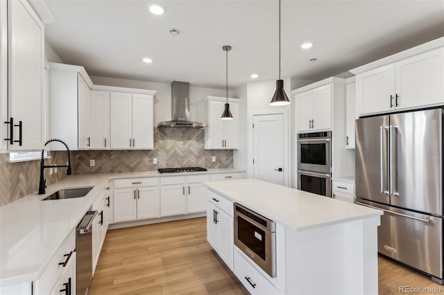 kitchen featuring a kitchen island, wall chimney range hood, appliances with stainless steel finishes, light wood-style floors, and a sink