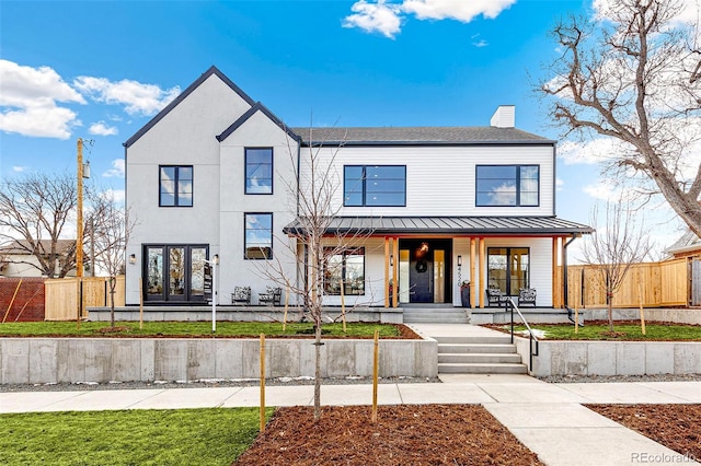 modern farmhouse featuring a chimney, a standing seam roof, fence, french doors, and a porch