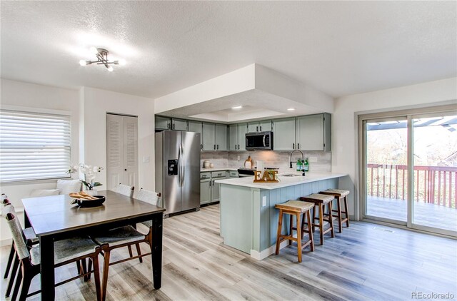 kitchen with a sink, light countertops, appliances with stainless steel finishes, a kitchen breakfast bar, and a peninsula
