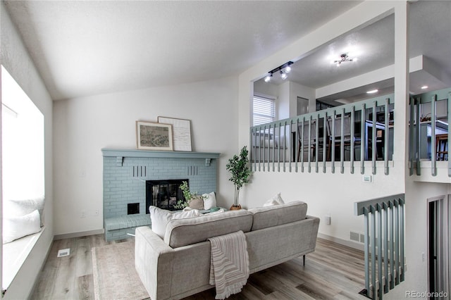 living room featuring a brick fireplace, wood finished floors, vaulted ceiling, and baseboards