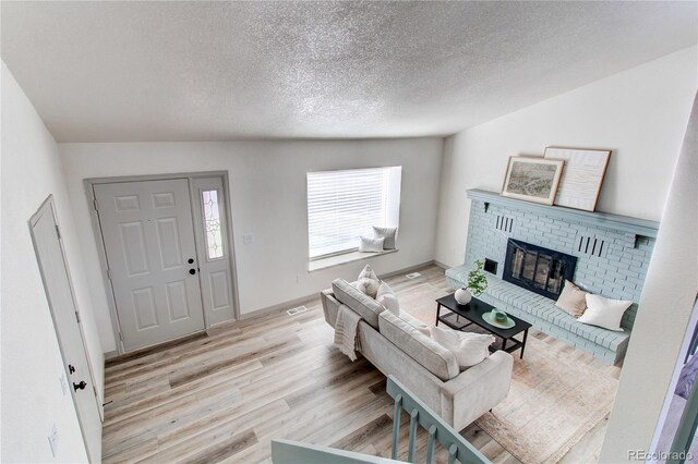 living area featuring visible vents, light wood-type flooring, a brick fireplace, and a textured ceiling