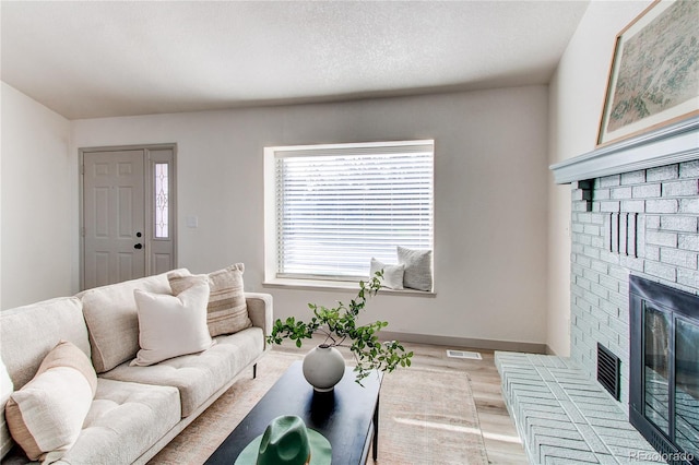 living area with visible vents, baseboards, a brick fireplace, a textured ceiling, and light wood-style flooring