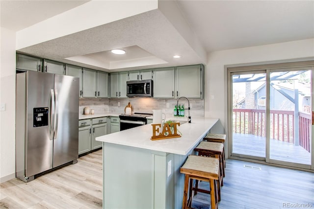 kitchen with a peninsula, backsplash, gray cabinetry, a raised ceiling, and stainless steel appliances