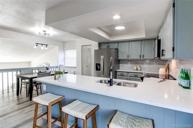 kitchen featuring a peninsula, tasteful backsplash, a sink, stainless steel appliances, and a raised ceiling