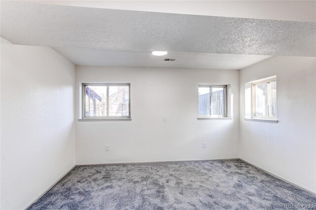 carpeted spare room featuring a textured ceiling, a healthy amount of sunlight, and visible vents