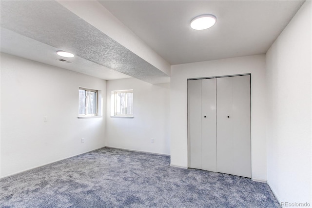 unfurnished bedroom with a textured ceiling, a closet, carpet flooring, and visible vents