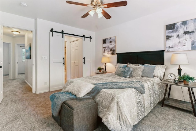 bedroom with light carpet, ceiling fan, ensuite bathroom, and a barn door