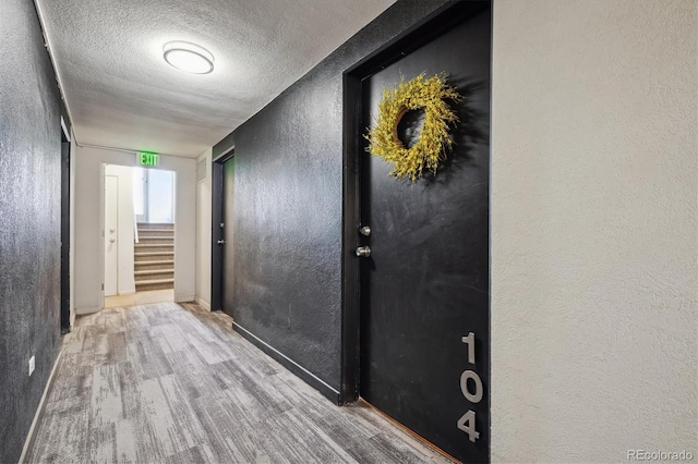 corridor with a textured wall, wood finished floors, a textured ceiling, stairs, and baseboards