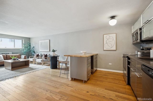 kitchen with appliances with stainless steel finishes, light wood-style flooring, a breakfast bar, and a peninsula