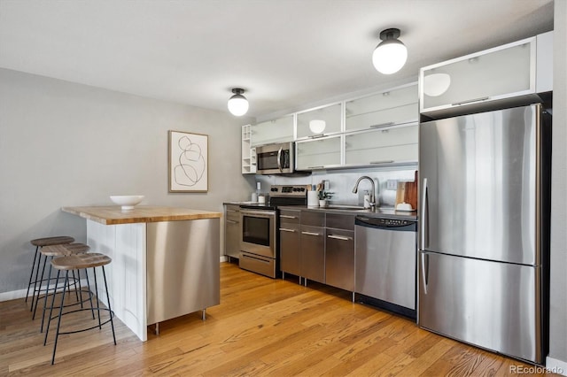 kitchen featuring stainless steel appliances, a sink, open shelves, a breakfast bar area, and light wood-style flooring
