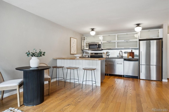 kitchen featuring appliances with stainless steel finishes, a peninsula, a sink, light wood finished floors, and a kitchen breakfast bar