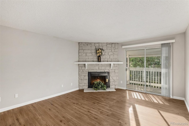 unfurnished living room with a textured ceiling, wood-type flooring, and a stone fireplace