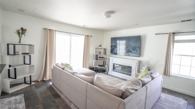 living room with a wealth of natural light, a glass covered fireplace, visible vents, and stone finish flooring