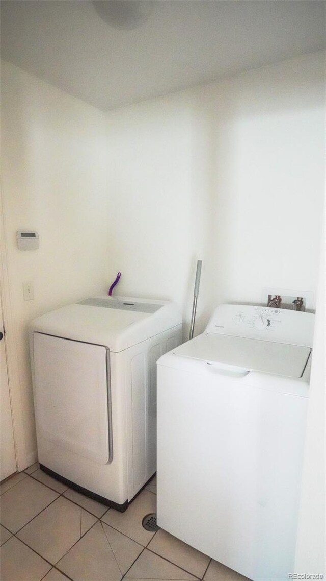 clothes washing area with laundry area, washing machine and clothes dryer, and light tile patterned floors