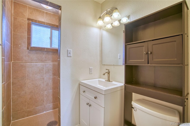 bathroom featuring vanity, a tile shower, and toilet