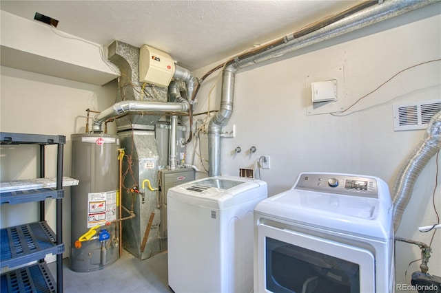 clothes washing area with heating unit, washing machine and dryer, a textured ceiling, and gas water heater