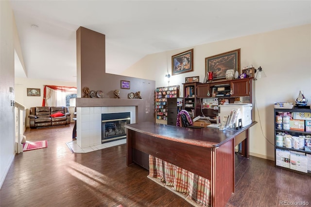 home office with dark wood-style floors, baseboards, vaulted ceiling, and a tiled fireplace