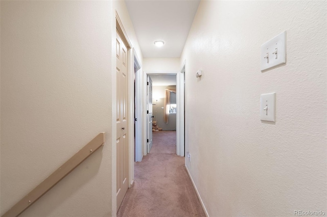 hallway with a textured wall, carpet, and baseboards