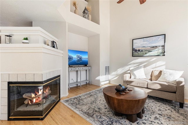 living room featuring a high ceiling, wood-type flooring, ceiling fan, and a fireplace