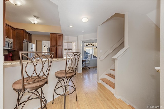 kitchen featuring appliances with stainless steel finishes, a breakfast bar area, light stone counters, kitchen peninsula, and light hardwood / wood-style flooring