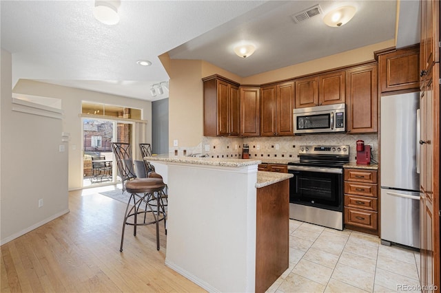 kitchen featuring a breakfast bar, appliances with stainless steel finishes, light stone counters, decorative backsplash, and kitchen peninsula