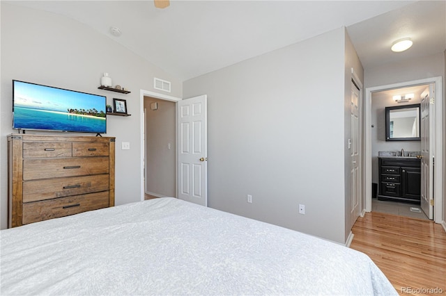 bedroom featuring vaulted ceiling, ensuite bath, sink, and hardwood / wood-style floors