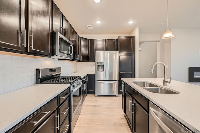 kitchen featuring decorative light fixtures, appliances with stainless steel finishes, a sink, light wood finished floors, and recessed lighting
