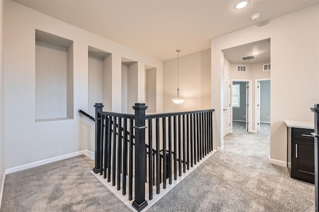 corridor featuring carpet floors, baseboards, visible vents, and an upstairs landing