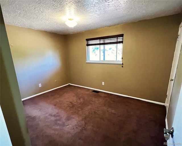 empty room with dark colored carpet and a textured ceiling