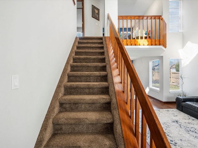 stairs with baseboards, a towering ceiling, and wood finished floors