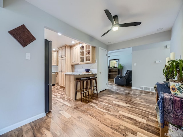 kitchen featuring light hardwood / wood-style flooring, a kitchen bar, ceiling fan, and light stone counters