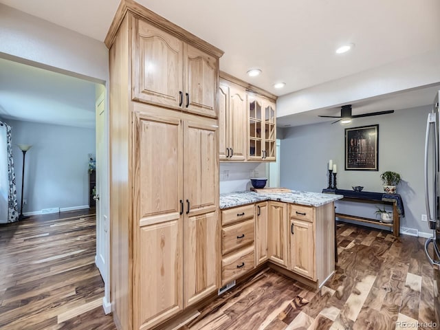 kitchen with light stone countertops, kitchen peninsula, dark hardwood / wood-style flooring, ceiling fan, and light brown cabinets