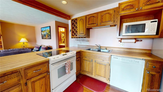 kitchen with a sink, a peninsula, brown cabinetry, white appliances, and open floor plan