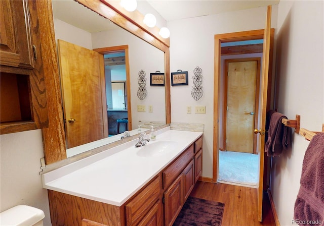 half bath with toilet, wood finished floors, and vanity