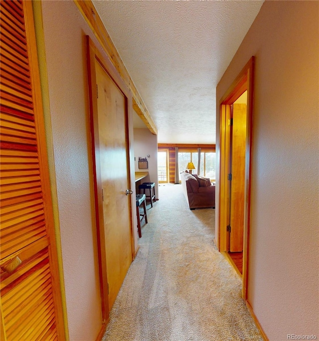 corridor featuring light colored carpet, a textured ceiling, and a textured wall