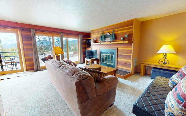 living room with wood walls, a glass covered fireplace, a healthy amount of sunlight, and carpet floors