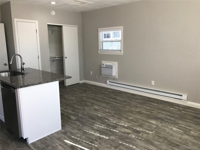 kitchen featuring a wall mounted air conditioner, dark stone counters, a baseboard heating unit, sink, and dark hardwood / wood-style floors