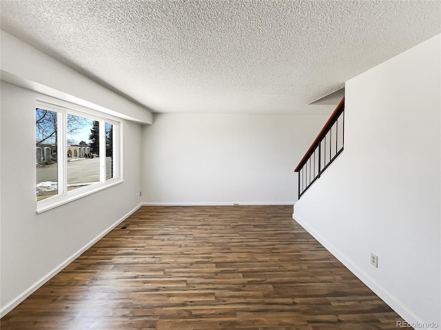 spare room with stairs, dark wood-style flooring, a textured ceiling, and baseboards