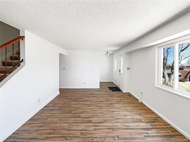 spare room featuring wood finished floors, a textured ceiling, baseboards, and stairs