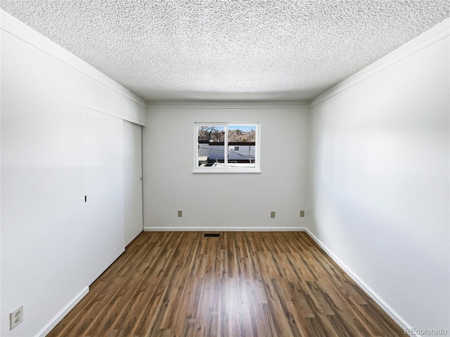 empty room with crown molding, visible vents, dark wood-type flooring, a textured ceiling, and baseboards