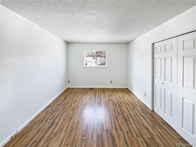 unfurnished bedroom with a closet, ornamental molding, a textured ceiling, wood finished floors, and baseboards