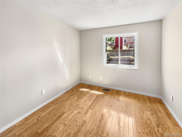 unfurnished room featuring visible vents, baseboards, a textured ceiling, and light wood-style flooring