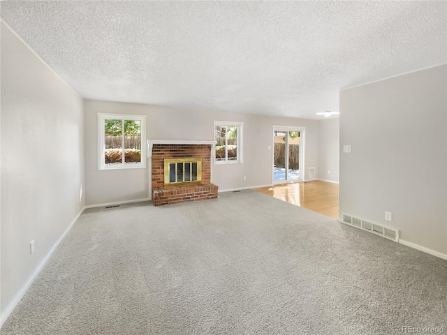 unfurnished living room featuring a brick fireplace, plenty of natural light, visible vents, and carpet floors