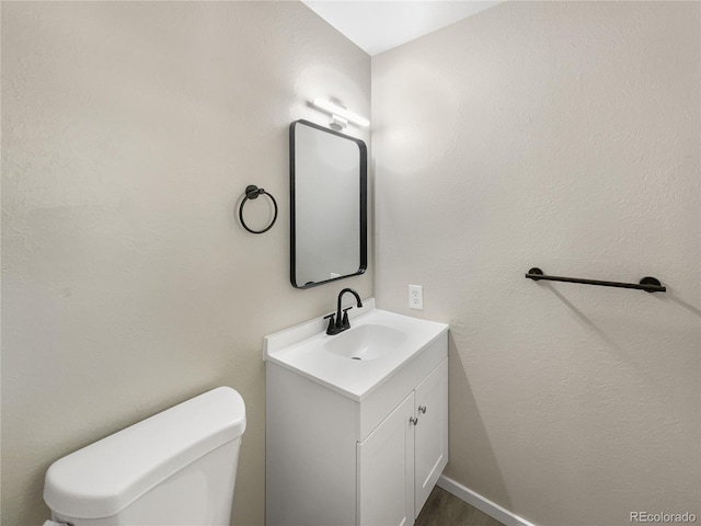 half bathroom featuring toilet, vanity, and baseboards