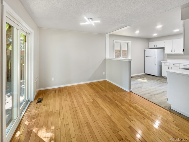 unfurnished living room with light wood-type flooring, visible vents, a textured ceiling, recessed lighting, and baseboards