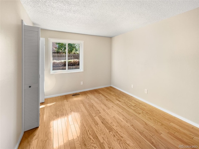 unfurnished room with a textured ceiling, visible vents, light wood-type flooring, and baseboards