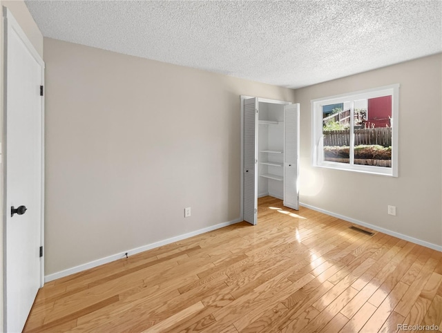 unfurnished bedroom with visible vents, a textured ceiling, light wood-type flooring, and baseboards