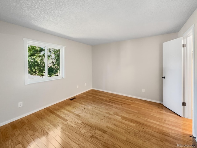 empty room with visible vents, baseboards, light wood-style floors, and a textured ceiling